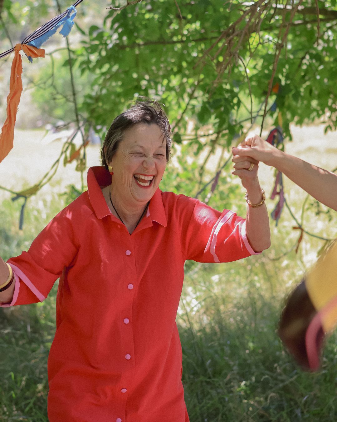 Elderly lady laughing in a red dress outdoors with greenery in the background